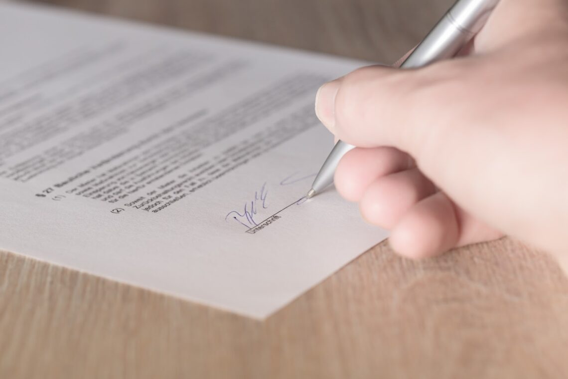 Hand signing a document with a pen.
