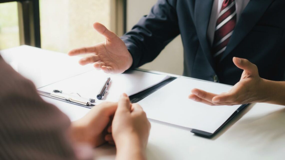 Hands of two people sitting across from one another with paperwork on a table between them.