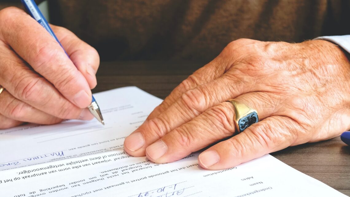 Hands of an elderly person signing a document.