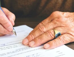 Hands of an elderly person signing a document.