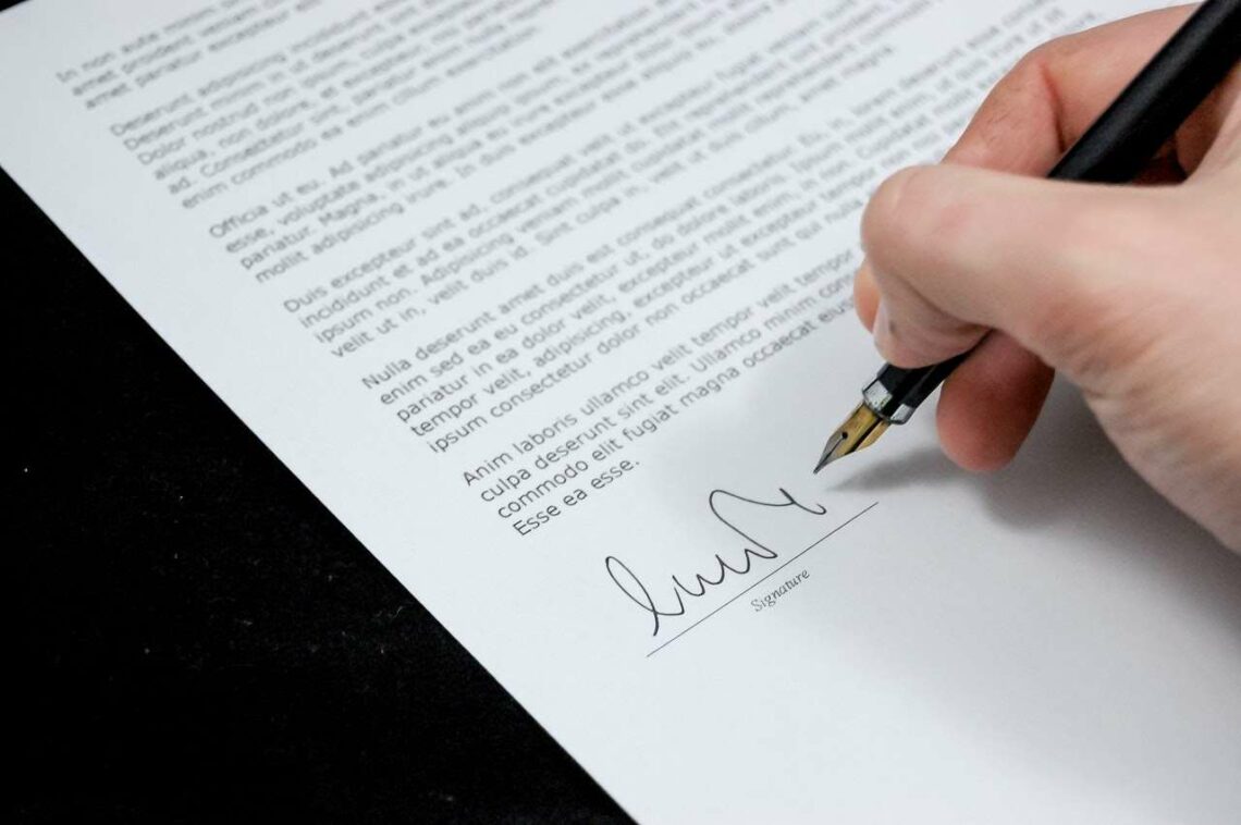 A hand signing a document with a black pen.