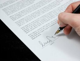 A hand signing a document with a black pen.