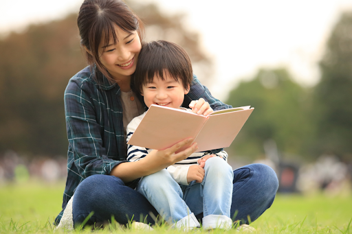 A mother and child reading a book together outside.