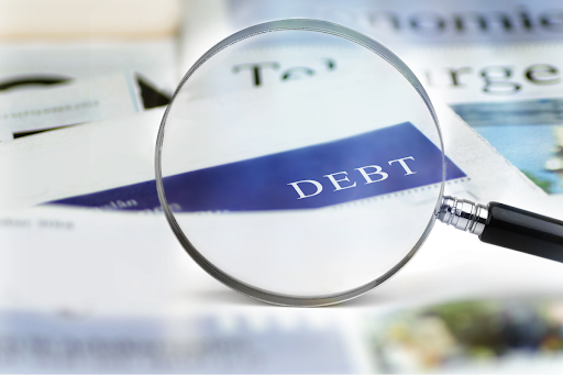 Magnifying glass showing the word DEBT on a stack of documents.