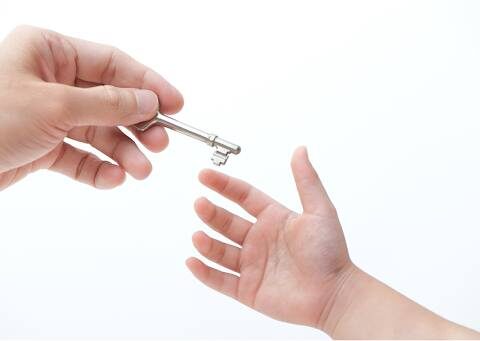 Adult's hand passing a key to a child's hand.