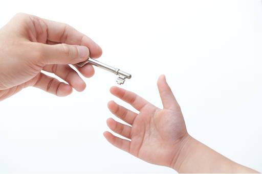 Adult's hand passing a key to a child's hand.