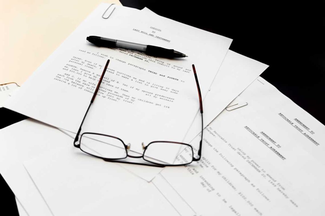 Multiple will and amendment documents on a table, glasses and a pen on top.
